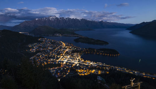 High angle view of illuminated city by sea against sky at night