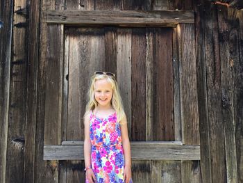 Portrait of happy girl standing against wooden cottage