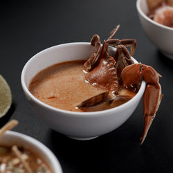 High angle of yummy whole boiled crab lying in tasty spicy tomato gravy in white ceramic bowl on gray table among other aromatic colorful dishes in modern restaurant