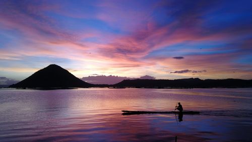 Silhouette person on sea against sky during sunset