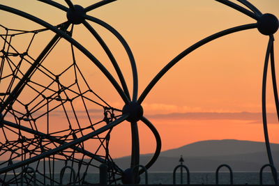 Silhouette of wrought iron fence against orange sky