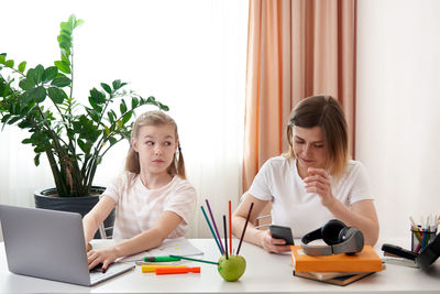 Mother and daughter sitting by desk at home