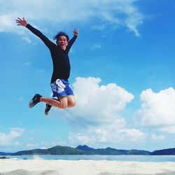 Full length of man with arms raised jumping at beach against sky