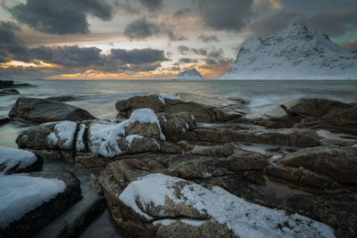 Scenic view of sea by snowcapped mountains against sky during sunset