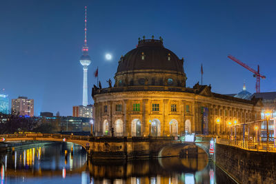 Illuminated buildings by river against sky in city at night