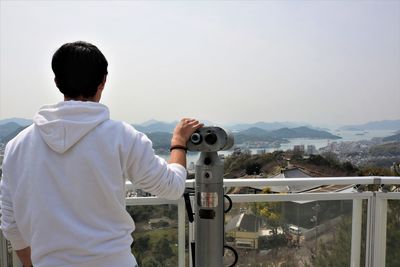 Rear view of man looking at cityscape against sky