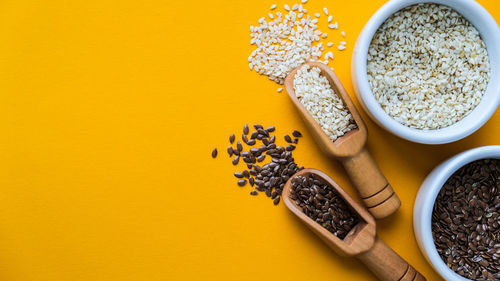 Wooden spoons with sesame and flax seeds lies in a white mortar on a yellow background. healthy eat