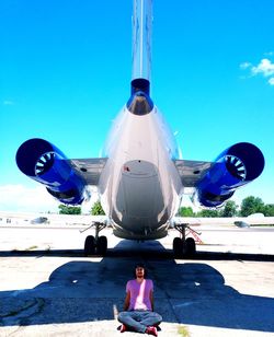 Portrait of man sitting against airplane at airport runway against sky