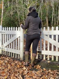 Rear view of woman standing by gate during autumn