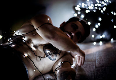 Shirtless man with illuminated string lights in dark