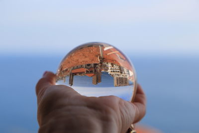 Cropped image of person holding glass ball with upside down reflection of town