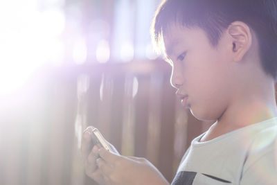 Close-up of boy using mobile phone in brightly lit room