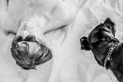 Directly above shot of shirtless man lying down by dog at beach