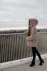 Side view of woman standing on railing against sky