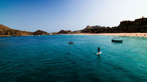 Rear view of man paddleboarding in sea against clear sky