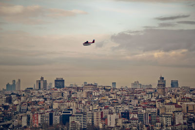 Airplane flying over cityscape against sky