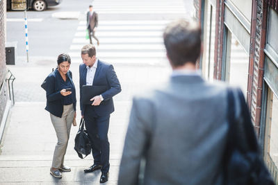 Male and female colleagues using phone on staircase in city