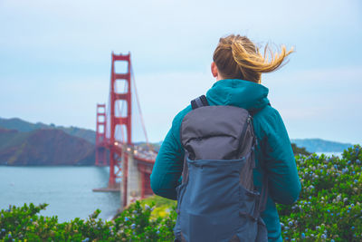Rear view of backpack woman standing against golden gate bridge