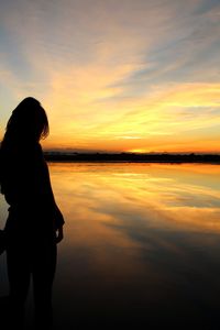 Silhouette woman standing by sea against sky during sunset