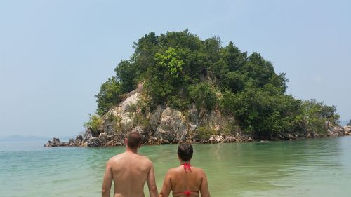 Rear view of couple by sea against rock formation