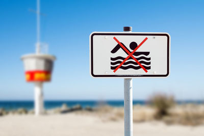 Close-up of no swimming sign at beach against sky