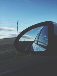 Road and sky reflecting in side-view mirror of car