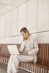 Woman using laptop while sitting on bench