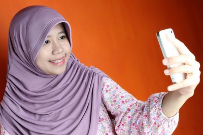Woman taking selfie standing against orange background