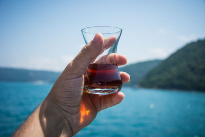 Close-up of hand holding alcohol against sea