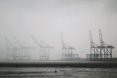 Cranes on pier over sea against sky