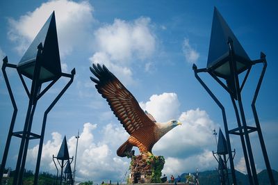 Low angle view of bird statue on blue sky and clouds