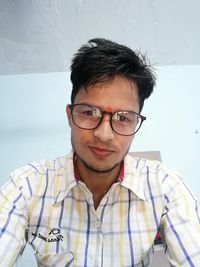Portrait of young man wearing eyeglasses against wall