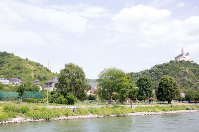 Scenic view of river by trees and building against sky