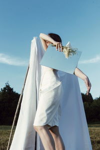 Woman holding umbrella standing on field against sky