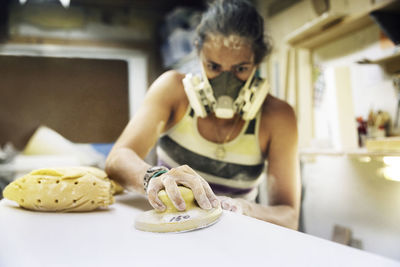 Woman using sander on surfboard in workshop