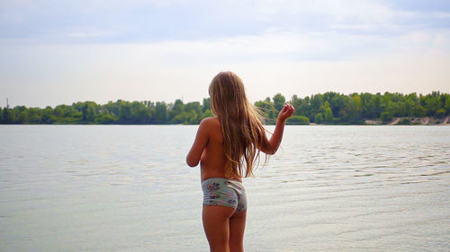 Rear view of young woman in bikini standing on beach against sky