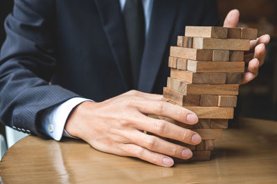 Midsection of businessman holding stacked wooden blocks on table