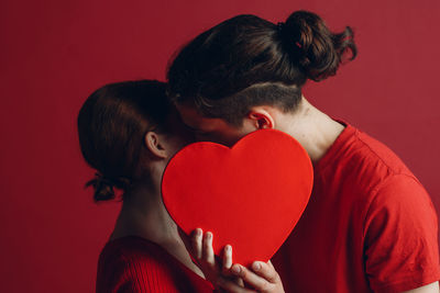 Midsection of woman holding heart shape against red background