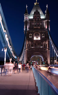 People walking on illuminated tower bridge at night