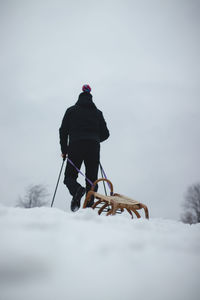 Man in black winter clothes pulls a wooden sledge to the top of the slope so he can go downstairs 
