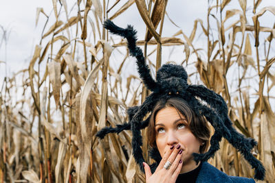 Woman covers mouth with hand in fear because of toy large spider on her head. halloween decorations