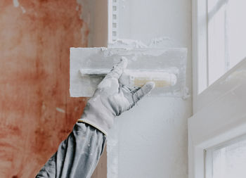 One hand in a construction glove a plasterer applies fresh putty on a window opening with a spatula