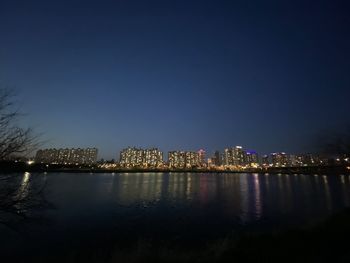 Illuminated buildings by river against sky at night