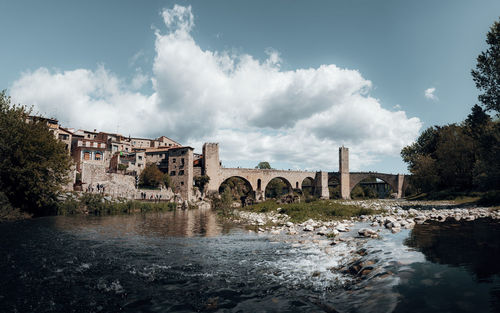 Bridge over river by buildings against sky