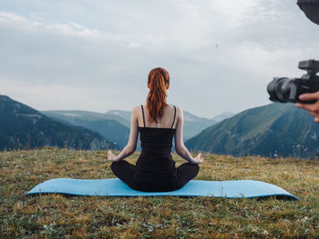 Woman sitting on seat in mountains against sky