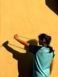 Shadow of girl with skipping rope on yellow wall