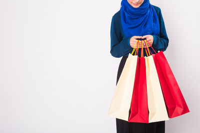 Rear view of woman holding shopping bags against white background