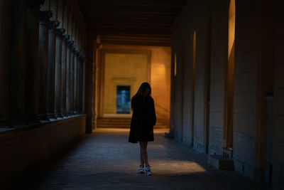 Full length of young woman standing in dark corridor