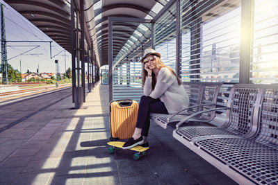 Portrait of smiling young woman sitting on bench at railroad station