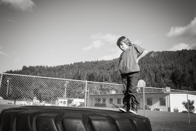 Portrait of boy making face while standing on tire against sky